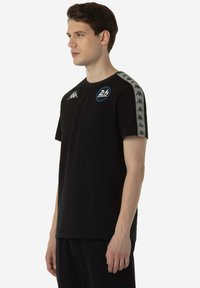 Zwart kort mouw T-shirt van katoen, met grijze strepen aan de zijkanten met logo's en een blauwe cirkelvormige afbeelding op de borst.