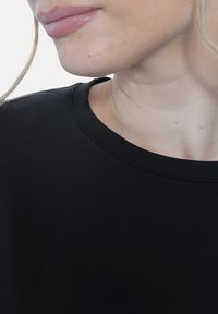 Zwart katoenen T-shirt met een ronde hals. Gladde textuur, minimalistisch ontwerp, met een close-up van de kraag en het bovenste schoudergebied.