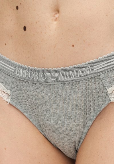 Κοντινό πλάνο του κάτω μέρους της κοιλιάς ενός ατόμου που φοράει γκρι ριμπεζέ εσώρουχα Emporio Armani με δαντελένιο τελείωμα και εμφανείς ελιές στο δέρμα.