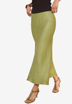 Hame green satin dengan tekstur halus, siluet yang pas, dan sedikit mekar di ujungnya, dipadukan dengan sandal hak tinggi berjalur hijau.