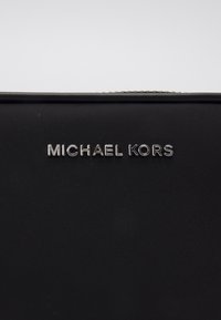 Tissu en nylon noir à la texture lisse, mettant en avant un logo "MICHAEL KORS" métallique argenté. Design simple et élégant.