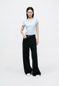 Light blue ribbed crop top with short sleeves and a small logo, paired with high-waisted black wide-leg pants and white sneakers.