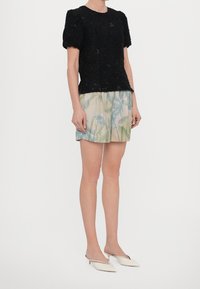 Maglietta nera a maniche corte con texture, abbinata a pantaloni corti di colore chiaro con una delicata stampa floreale verde e blu. La modella indossa mule bianche.