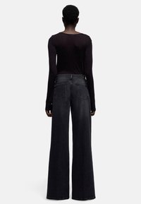 Zwart denim met wijde pijpen en een hoge taille, uitgevoerd met een klassiek ontwerp met vijf zakken en subtiele stikseldetails. Strak zittend top met lange mouwen.