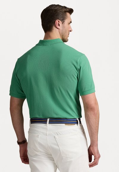 Grønn polo skjorte med teksturert overflate, korte ermer og klassisk krage, kombinert med hvite bukser og et flerfarget stripet belte.