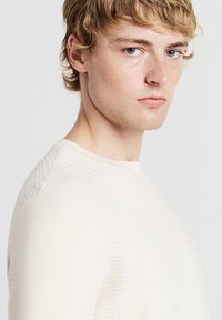 Maglione beige chiaro texturizzato con scollo rotondo e silhouette aderente, caratterizzato da sottili dettagli a coste sulle spalle e sulle maniche.