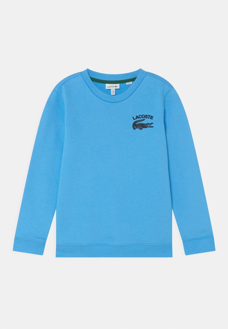Chemise à manches longues bleu clair avec logo crocodile Lacoste noir et texte sur le côté gauche de la poitrine.