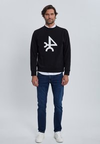 Sudadera negra con un diseño gráfico blanco en el frente, combinada con jeans azules y zapatillas blancas. Corte casual, material de algodón.