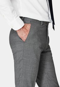 Pantaloni grigi su misura realizzati in tessuto testurizzato, dotati di tasche laterali e un design leggermente affusolato. Indossati con una camicia bianca.
