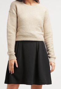 Vaatteena on vaaleanbeige raidallinen neulepaita pitkillä hihoilla, joka on yhdistetty mustaan, laskostettuun hameeseen. Molemmilla vaatteilla on pehmeä texture ja yksinkertainen muotoilu.