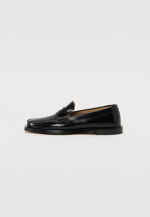 Black leather loafers with a rounded toe, decorative stitching, and a flat sole. Smooth texture and minimalistic design.