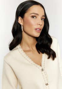 Cardigan color crema con scollatura a V, impreziosito da dettagli in perline lungo il décolleté e due bottoni decorativi sul davanti.