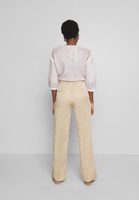 Witte, gestructureerde gebreide top met driekwart mouwen, gecombineerd met beige, hoge taille wijdvallende broek met achterzakken.