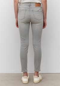 Jeans ajustados grises de cintura alta, con textura de denim y bolsillos traseros. Incluye una etiqueta de parche de cuero marrón claro en la cintura.