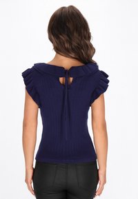 Top din tricot navy cu nervuri, cu mâneci volanate, spate deschis și detaliu cu fundiță la gât. Siluetă ajustată cu țesătură texturată.