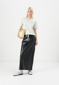 Črtasta krema in črno bombažna majica, črna usnjena maksi krila, svetlo rumena torbica in sivi slip-on čevlji v minimalističnem okolju.