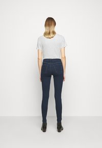 Jeans ajustados de color azul oscuro hechos de denim, con una cintura alta, bolsillos traseros estándar y una textura suave y sin adornos. Combinados con una camiseta gris y botas negras hasta el tobillo.