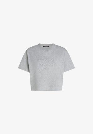 Camiseta gris cortada hecha de una tela suave, con cuello redondo y mangas cortas, que presenta un diseño de logo en relieve en la parte frontal.