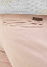 Ružičaste hlače imaju stražnji džep s dizajnom proreza i Jack & Jones oznaku, smještene na teksturiranoj svijetlosivoj tkanini.