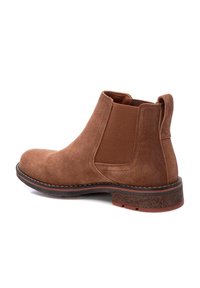 Botas de tobillo de ante marrón con paneles elásticos en los laterales, puntera redondeada y un tacón bajo. Detalle de costura a lo largo de la suela y suela de goma texturizada.