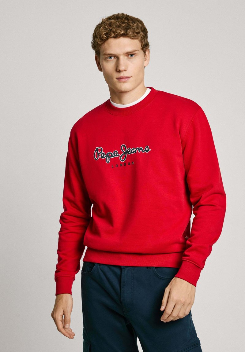 Rdeča majica s dolgimi rokavi, okroglim ovratnikom in črnim logotipom "Pepe Jeans London". Tkanina se zdi mehka z gladko teksturo.
