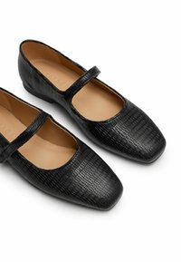 Zapatos Mary Jane de cuero negro con un acabado texturizado, puntas cuadradas y una única correa en el empeine. Tacón plano.