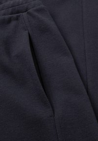 Tmavě modré tepláky s detailním záběrem na texturu látky, s hladkým povrchem a bočním švem, který obsahuje kapsu.