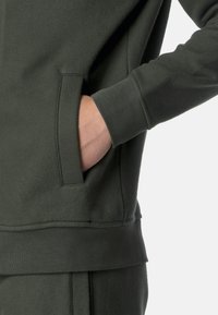 Felpa verde scuro con tasca frontale, polsini a costine e tessuto morbido e testurizzato, dal taglio rilassato.