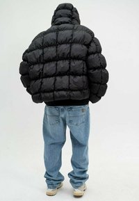 Doudoune noire avec texture matelassée et col montant, associée à un jean bleu clair ample et des baskets neutres.
