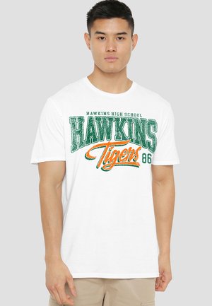 White cotton t-shirt featuring green and orange "Hawkins High School Tigers 86" graphic print. Short sleeves and crew neck design.
