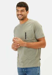 Lys grøn t-shirt med korte ærmer og en brystlomme med en sort lynlås. Blødt stof, simpel design og afslappet pasform.