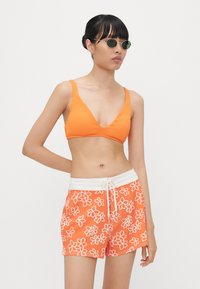 Oranje geribbelde bikini top, gecombineerd met oranje zwemshorts met een wit bloemenpatroon en een witte trekkoord taille.