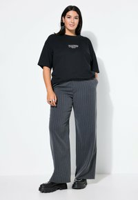 Černé oversized tričko s bílým potiskem, spárované se šedými proužkovanými širokými kalhotami a masivními černými platformovými botami.