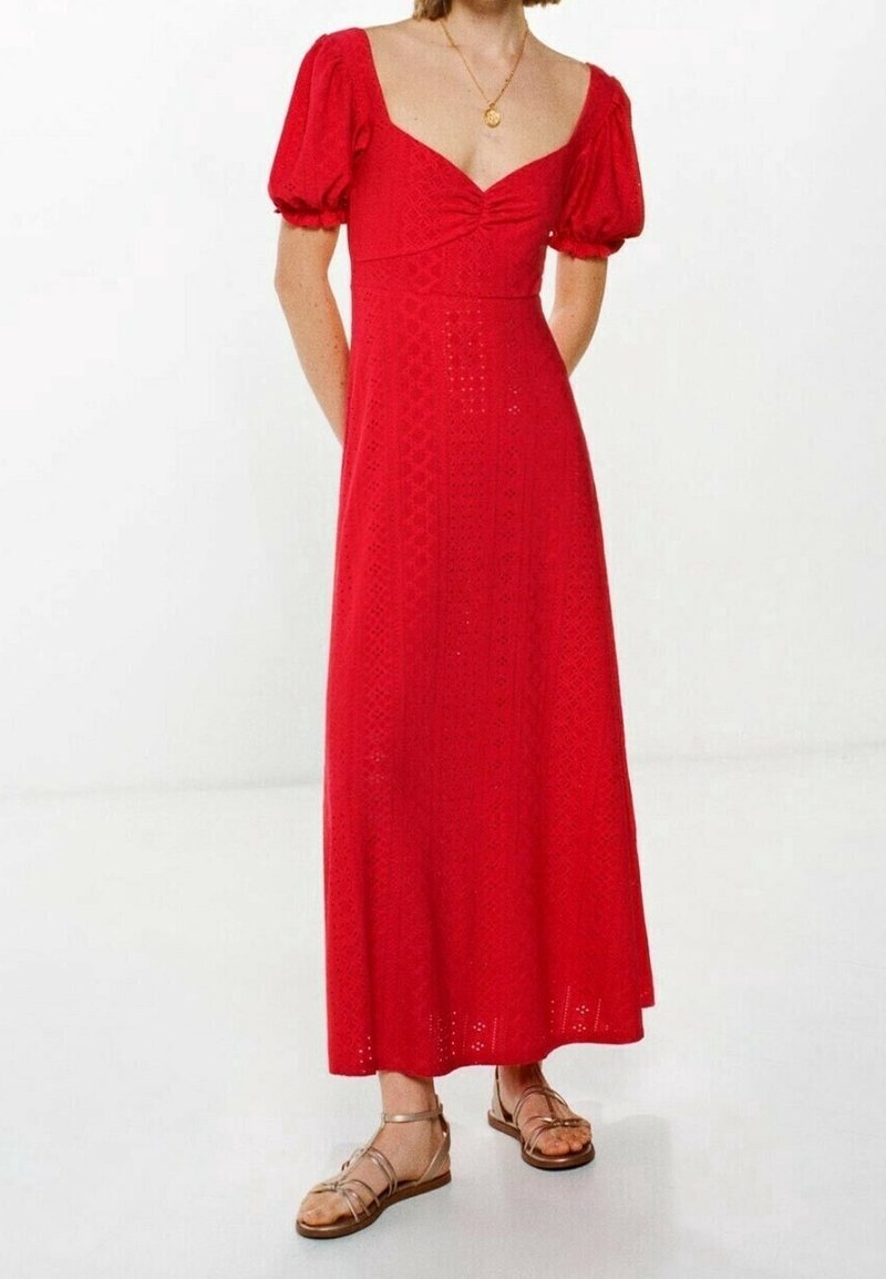 Robe maxi rouge avec manches courtes bouffantes, encolure carrée, motif géométrique texturé et ourlet évasé. Portée avec des sandales à brides marron.