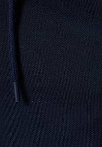 Navyblauwe sweatshirtstof met een fijn, gestructureerd breisel. Een gevlochten trekkoord met een plastic punt is zichtbaar langs de rand.