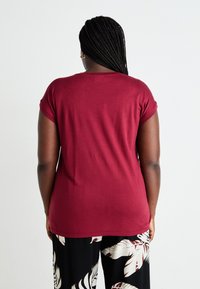 Maroon t-shirt, short sleeves, soft fabric, relaxed fit, solid color; paired with black pants featuring a white tropical leaf pattern.