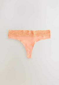 Meka pamučna tanga donje rublje u boji breskve s rubom od cvjetnog čipka i glatkim prednjim dijelom, položena ravno na svijetloj podlozi.