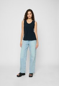 Top sans manches bleu marine avec des plis, bretelles en dentelle décoratives ; associé à un jean en denim bleu clair et ample et des sandales à plateforme noires.