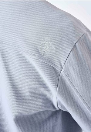Camicia in tessuto grigio chiaro con una texture a coste; presenta un logo ricamato sulla spalla. Il taglio offre una vestibilità moderna.