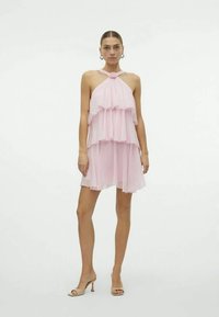 Abito halter rosa chiaro con strati di rouches, texture trasparente e scollatura annodata. Ha una vestibilità morbida e arriva sopra il ginocchio.