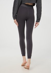 Ciemnoszare legginsy o gładkiej fakturze, z wysokim stanem i dopasowanym krojem zwężającym się w kostkach. Widać minimalne detale szwów.