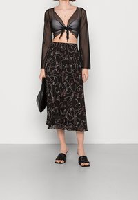 Paita musta, sheer, cu mâne lungi, combinată cu o fustă neagră cu un model abstract colorat. Sandale negre țesute și o geantă texturată neagră completează look-ul.