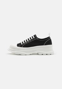 Schwarze Leinensneaker mit weißer Gummisohle, abgerundeter Zehenkappe und weißen Schnürsenkeln. Auffällige strukturierte Sohle und seitliche Nähdetails.