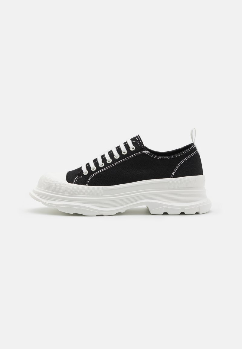 Schwarze Leinensneaker mit weißer Gummisohle, abgerundeter Zehenkappe und weißen Schnürsenkeln. Auffällige strukturierte Sohle und seitliche Nähdetails.