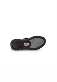 La semelle de chaussure présente une base en caoutchouc noir avec un insert gris texturé, une zone centrale lisse et une étiquette de logo au centre.