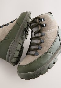 Grau-grüne Wanderschuhe aus synthetischem Leder und Wildleder, mit gummierten Profillaufsohlen, Metallösen und verstärkten Nähten.