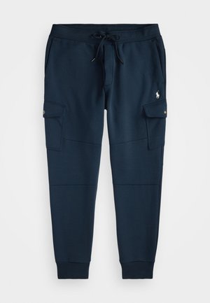 Tamsiai mėlynos spalvos cargo tipo džinsai su raišteliu juosmens srityje, šoninėmis kišenėmis su sagomis, rišamais manžetais ir mažu baltu išsiuvinėtu logotipu ant šlaunies.