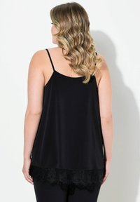 Camisole nera in satin con sottili spalline, caratterizzata da un orlo in pizzo. Il retro è liscio con una silhouette fluida e un design leggermente svasato.
