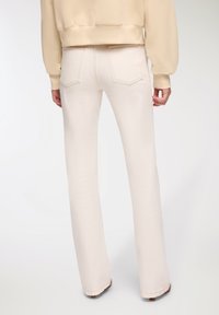 Jasno beżowe dżinsy z wysokim stanem i rozszerzanymi nogawkami, z subtelnymi przeszyciami i dwiema tylnymi kieszeniami, połączone z kremowym, krótkim swetrem.