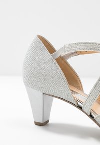 Scarpa con tacco argentato, con tomaia testurizzata e fascia elastica. Presenta un tacco chunky e un accento metallico lucido alla base.